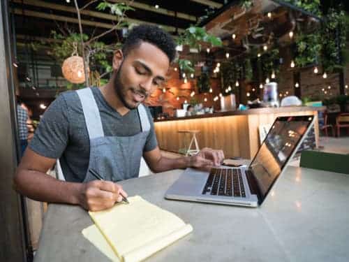 man working on laptop and taking notes