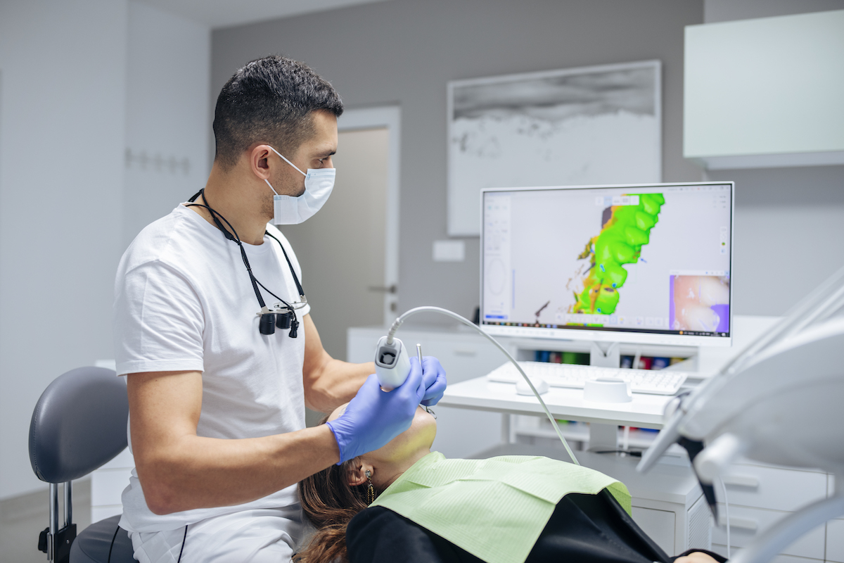 Dentist in medical clinic using a new modern 3D dental scanner on young female patient. The dental practice is protected from cyber threats.