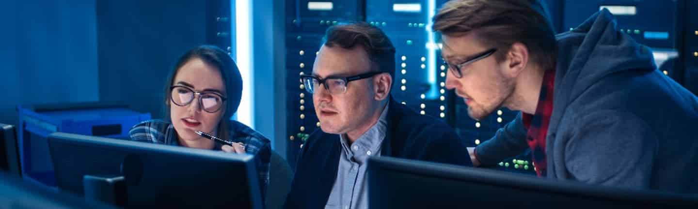 three people looking at computers in a data center