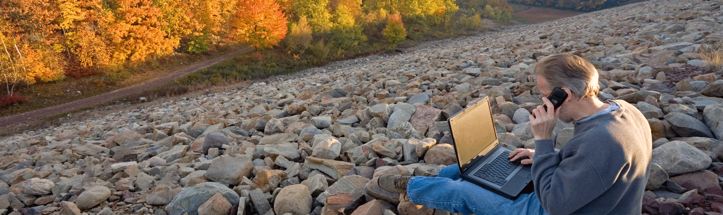 man sitting on rocks with computer